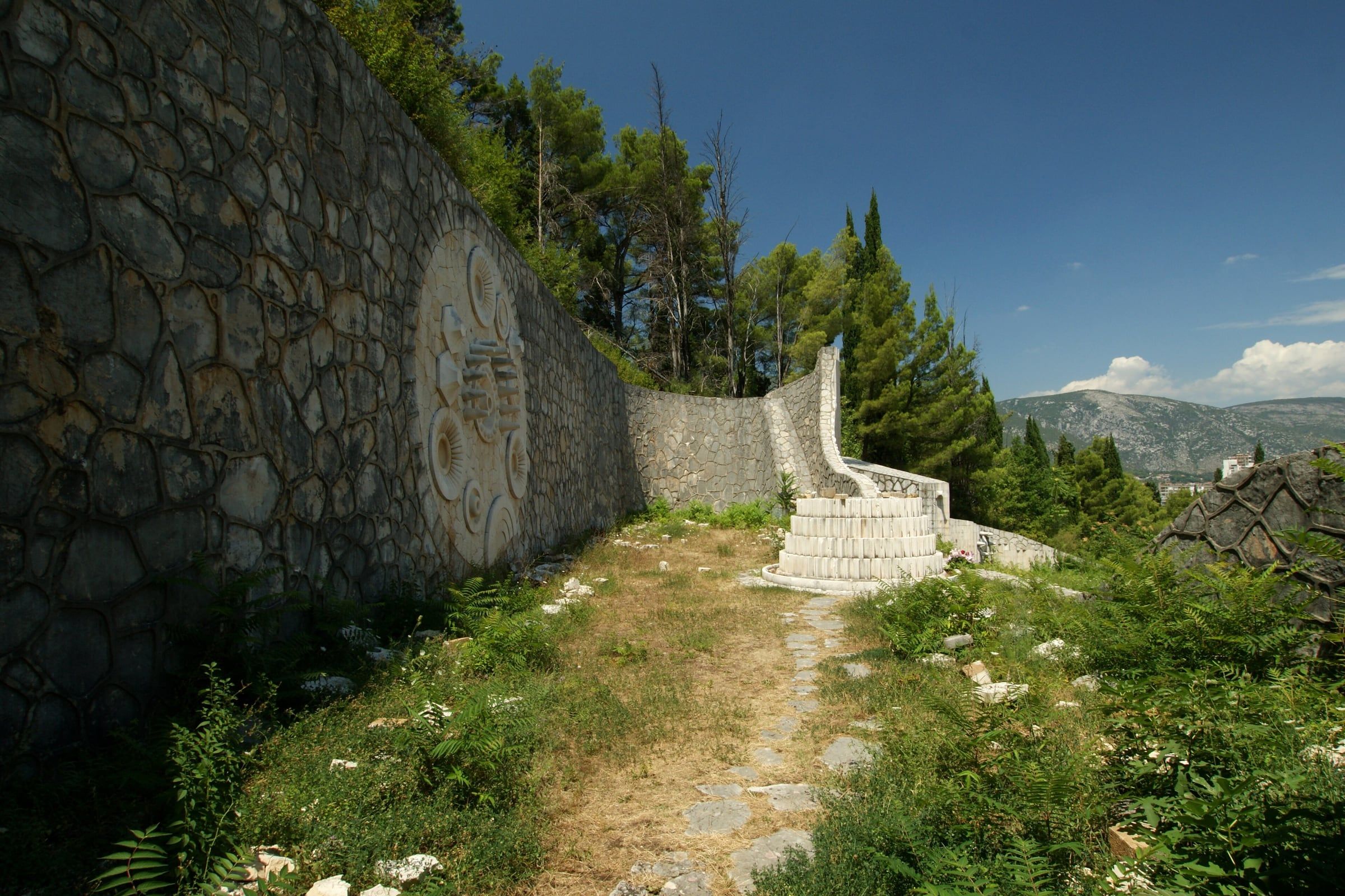 A stone path climbing between terraced stone walls carved with circular motifs at the Partisan Memorial Cemetery.